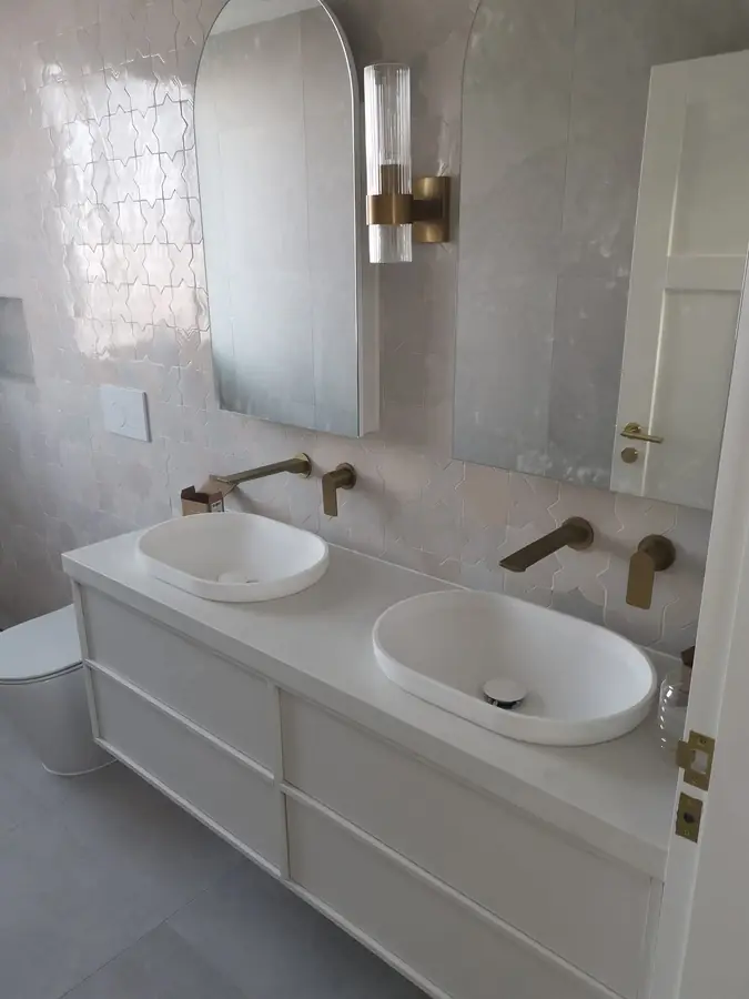 Arabesque tiled bathroom wall with arched mirrors and brushed brass tapware