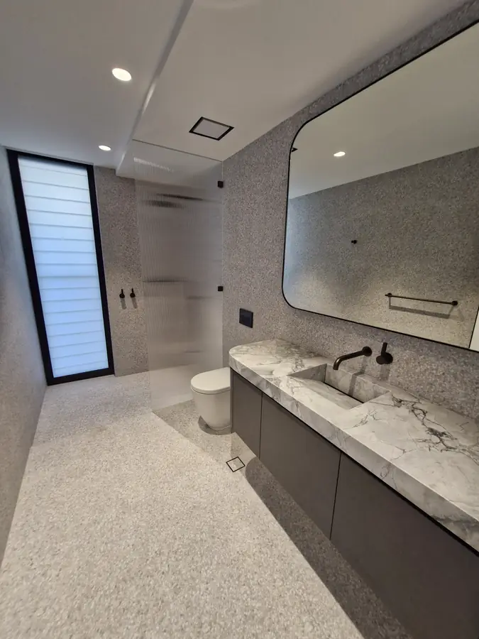 Renovated bathroom in Sydney with a dark marble vanity, black-framed mirror and matte grey wall tiles